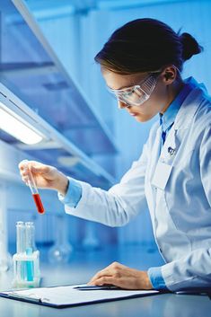 a woman in white lab coat and goggles holding a test tube with liquid on it