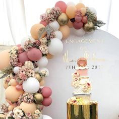 a wedding cake surrounded by balloons and flowers on top of a gold pedestal with a sign that reads engagement of mardi gras