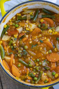 a yellow pot filled with vegetable soup on top of a wooden table next to a white napkin