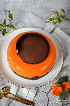 an orange and white plate with a chocolate dessert on it next to some gold spoons