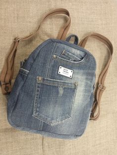 Introducing the perfect combination of style, sustainability, and functionality - our handmade denim backpack. Made with recycled jeans and a 100% cotton lining, this backpack is not only fashionable but also environmentally friendly. With 5 pockets on the outside and 2 deep pockets on the inside, you'll have plenty of space to organize your belongings. The strong webbing straps ensure durability, while the label and genuine leather on the zipper puller add a touch of elegance. Measuring approximately 30 cm in height, 25 cm in width, and 12 cm at the bottom, this backpack is the perfect size for your daily adventures. Inside, the cotton lining is motley, adding a unique and playful touch. Upgrade your backpack game with this one-of-a-kind denim backpackbackpack. Denim Travel Backpack With Pockets, Travel Backpack With Pockets In Denim, Denim Blue Backpack With Pockets For Everyday Use, Denim Backpack With Pockets For Everyday Use, Denim Blue Cotton Backpack For Everyday Use, Denim Standard Backpack With Zipper Closure, Standard Denim Backpack With Pockets, Denim Backpack With Pockets, Denim Backpack With Zipper Closure