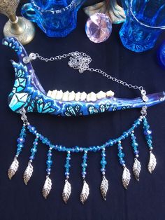 This is a Beautiful Painted, Blue and Purple Crystal Deer Jawbone Necklace! The Colors Here Are Just Fantastic! The Painted crystals Are a Light Blue Color And The Backdrop is Purple! A few rhinestones as well. Hanging from the bottom is a Bib of Glass beads! All 6 Teeth Are in perfect condition. The Whole Jaw Bone is 9 inches long. Also coated with polyurethane for the beautiful shine. The Chain is 20 inches long. All Items Ship Within 1-3 Days via USPS First Class Service. Shipping on This Bon Artistic Blue Jewelry For Festivals, Artistic Blue Necklaces For Festivals, Artistic Blue Necklace For Festivals, Handmade Blue Fantasy Jewelry, Blue Fantasy Jewelry For Jewelry Making, Fantasy Blue Jewelry For Jewelry Making, Painted Crystals, Real Bone Jewelry, Wiccan Necklace