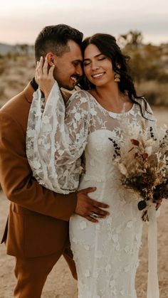 a bride and groom embracing each other in the desert with their arms around each other