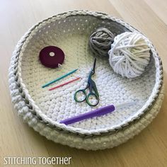 a crocheted bowl with yarn, scissors and knitting needles