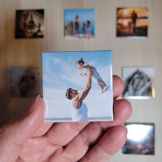 a person holding up a polaroid with pictures on the wall in the back ground