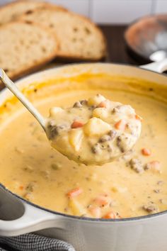 a ladle full of soup with bread in the background and a spoon holding it