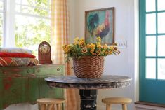 a table with two stools and a basket on it in front of a window