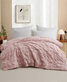 a bed with pink comforter and pillows in a white room next to a window