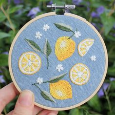 someone is holding up a embroidery project with oranges and lemons on blue background