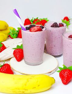 two glasses of smoothie with strawberries and banana on the side, surrounded by other fruit