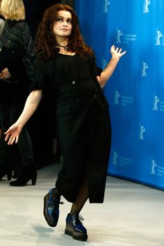 a woman with red hair and black dress walking on the runway in front of a blue backdrop