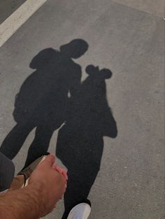 the shadow of a man and woman holding each other's hand while standing in an empty parking lot