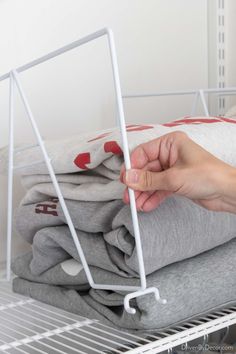 a person holding onto some folded clothes on a rack in a room with white walls