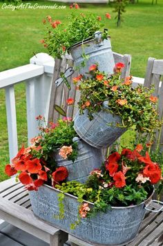 two metal buckets filled with flowers sitting on top of a wooden bench in the grass