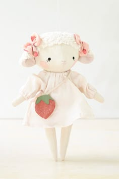 a stuffed animal wearing a white dress and holding a strawberry hanging from a string on a wall