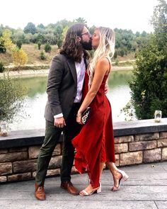 a man and woman kissing each other while standing next to a river