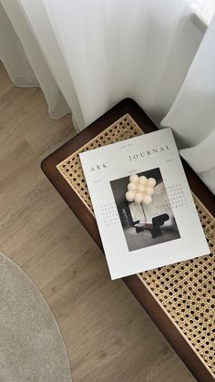 a magazine sitting on top of a wooden table next to a white curtain and chair