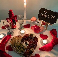 a table topped with a heart shaped platter filled with food and wine next to a lit candle