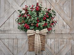 a basket filled with red berries and greenery on top of a wooden wall next to a door