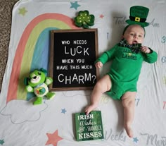 a baby laying on top of a blanket next to a chalk board with a sign that says who needs luck when you have this much charm?