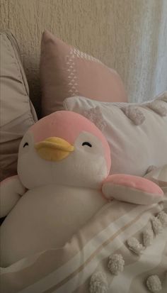 a stuffed penguin sitting on top of a bed next to pillows