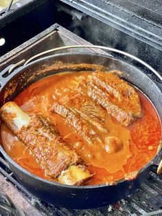 some meat is cooking on the grill in a pan with sauce and spoons next to it