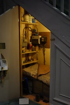 an open door leading to a small bed in a room with stairs and shelves on the wall