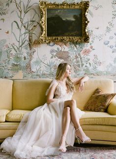 a woman sitting on top of a couch next to a painting