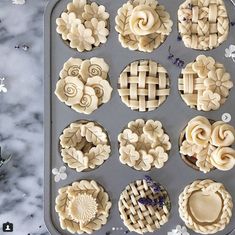 twelve pies are arranged in the shape of flowers on a baking tray with lavender sprigs