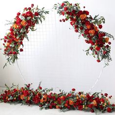 an arrangement of red and orange flowers arranged on a white backdrop with greenery in the middle