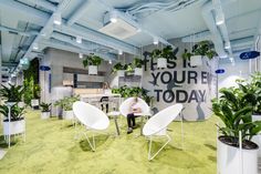 a man sitting in a chair next to some potted plants on the floor and a sign that says it's your today