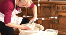 a woman in an apron working on a pottery wheel with her hands and knees bent over the wheel