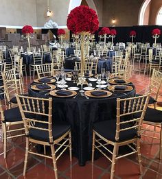 tables and chairs are set up with black linens, gold rimmed centerpieces, and red roses