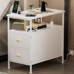 a night stand with two drawers and an alarm clock on the nightstand next to a bed