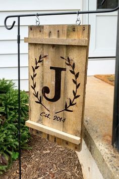 a wooden sign with the letter j on it hanging from a black metal pole in front of a house