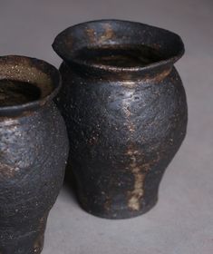 two black vases sitting next to each other on a gray tableclothed surface