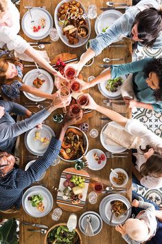 a group of people sitting around a wooden table with plates and bowls of food on it