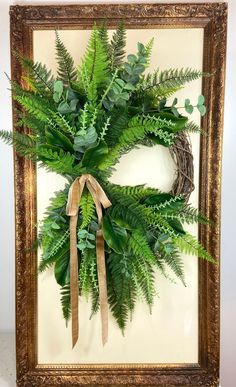 a wreath is hanging on the wall in front of a frame with a brown ribbon