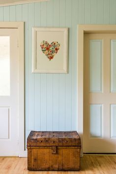 an old trunk is sitting in front of two doors and framed pictures on the wall