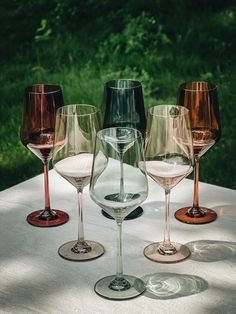 five wine glasses are lined up on a table outside with grass in the back ground