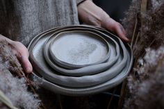 a person holding a stack of plates in their hands with dried grass around them and one hand on the plate