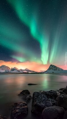 the northern lights shine brightly over water and rocks in front of snow covered mountain tops