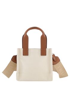 The oversized logo stamps a signature finish on a squared mini tote bag with leatherette top handles to comfortably weekend essentials in style. 18" H x 7" W x 4" D Magnetic top closure Exterior has front snap pocket Cotton/polyester with faux leather trim Lined Imported Beige Canvas Shopping Bag With Adjustable Handle, Rectangular Tan Bags For On-the-go, Trendy Rectangular Canvas Bag For On-the-go, Canvas Satchel Bag With Adjustable Handle For Shopping, Trendy Rectangular Canvas Bag With Adjustable Handle, Adjustable Handle Satchel Canvas Bag For Shopping, Adjustable Handle Canvas Satchel For Shopping, Trendy Rectangular Canvas Bag With Top Carry Handle, Trendy Rectangular Canvas Bag With Top Handle