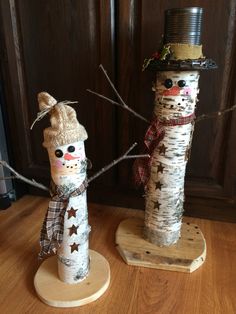 two snowmen made out of birch trees are standing on wooden bases, one is wearing a hat and the other has a scarf