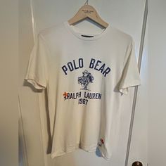 Polo Bear Graphic Tee. Super Soft Cotton, Ivory Body With “Ranch Bear” Graphic On Front, “Hand Written” Script And Embroidered Embellishments On Front And Back. Custom-Fit Medium. Nwot. Never Been Worn. Cream Casual Tops With Embroidered Logo, Casual Cream Tops With Embroidered Logo, White Embroidered Graphic Tee, Classic Cotton Top With Embroidered Graphics, Classic Embroidered Cotton Tops, Casual White Tops With Embroidered Logo, Classic Embroidered Short Sleeve Top, White Casual Shirt With Embroidered Logo, White Casual Shirt With Embroidered Graphics