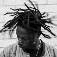 a man with dreadlocks standing in front of a brick wall looking at his cell phone