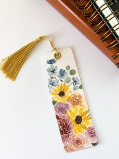 a bookmark with flowers painted on it and a tassel hanging from the end