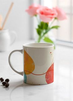 a white coffee cup sitting on top of a counter next to a vase filled with flowers