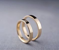 two gold wedding rings sitting on top of each other in front of a gray background