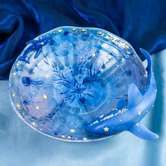 a blue glass bowl with gold stars and sea creatures painted on the bottom, sitting on a blue satin surface